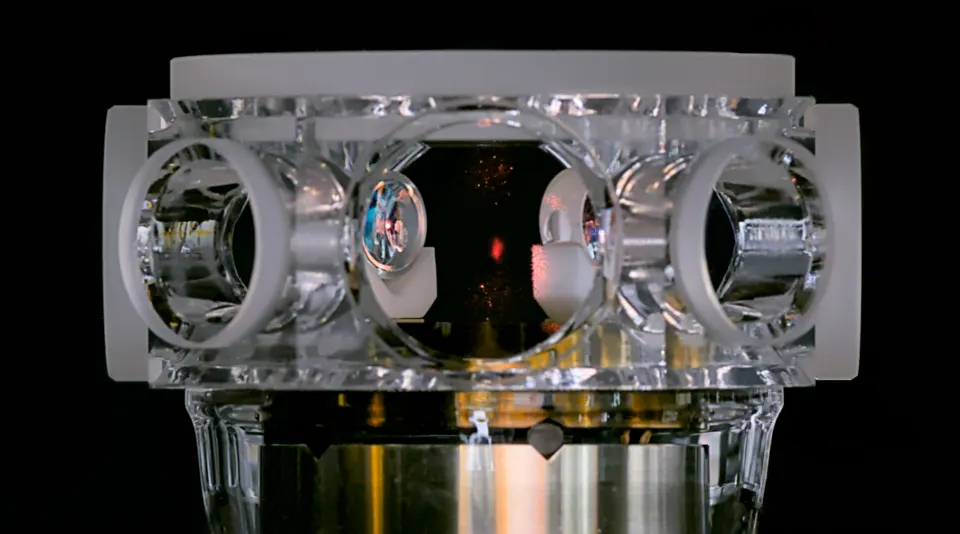 A glass vacuum cell with a glowing cloud of trapped atoms (red dot), not Atom Computing's: lasers cool atoms here before loading them into tweezers
