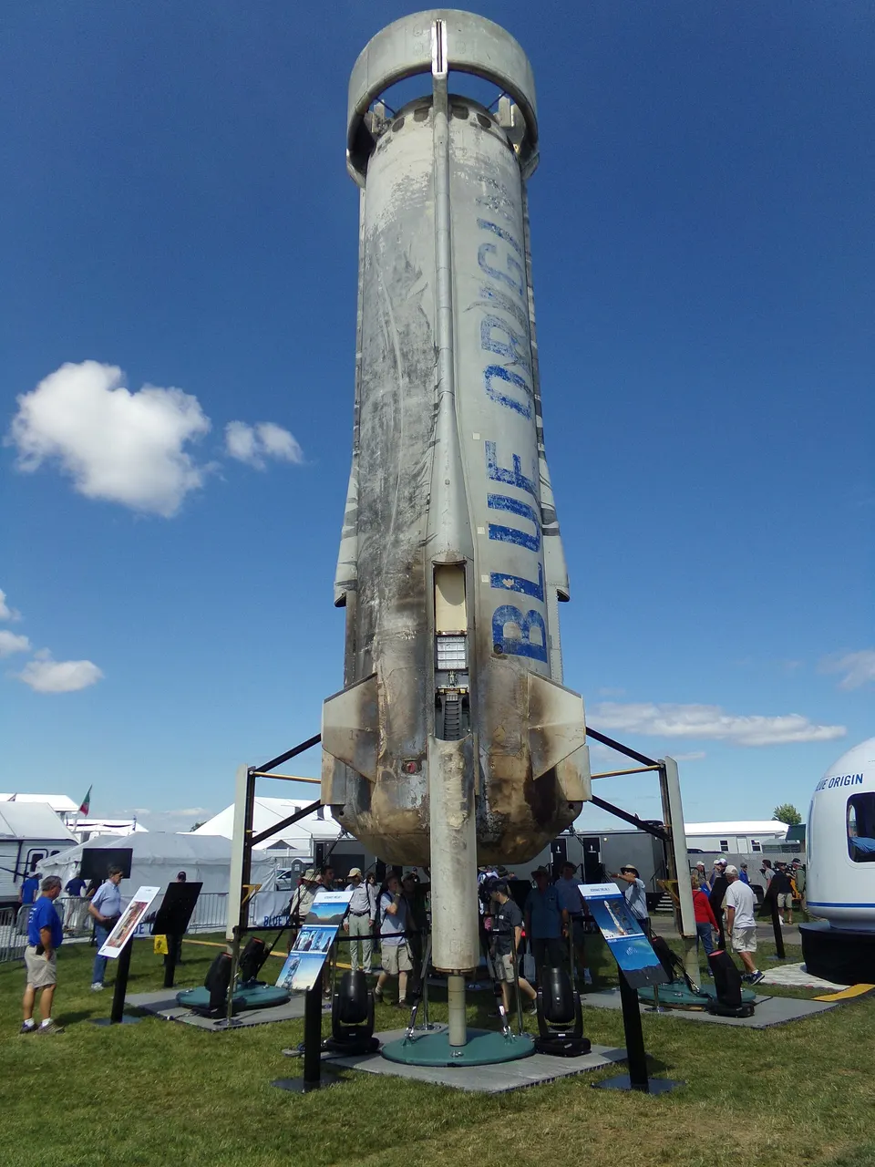 A flown New Shepard booster, scorched from reentry: the ring and fins at the top steer its fall, the legs at the base land it