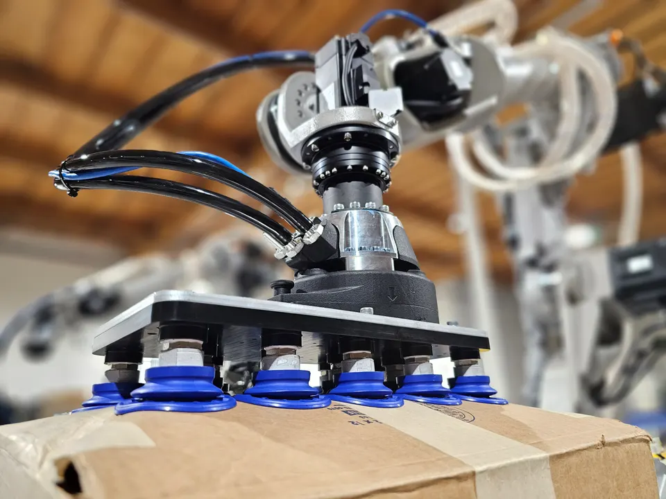 One of Mech's two arms gripping a box with a suction-cup pad; force sensing lets it press boxes into place and feel bumps