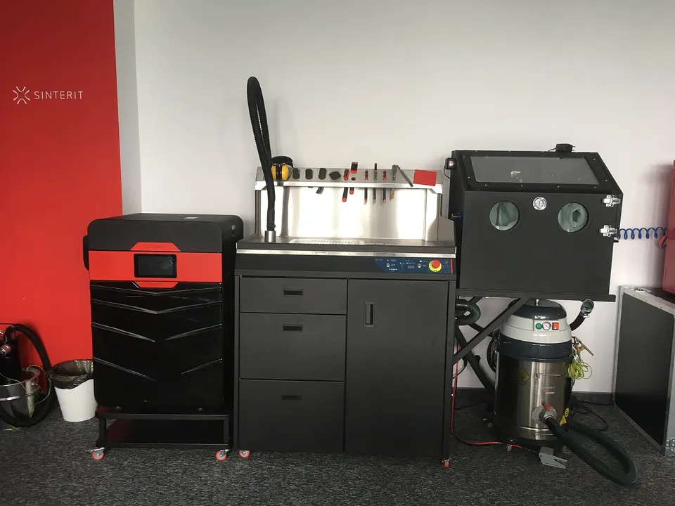 A compact nylon-powder (SLS) printer, left, beside its powder station where parts are dug out and loose powder recycled, as with the Fuse