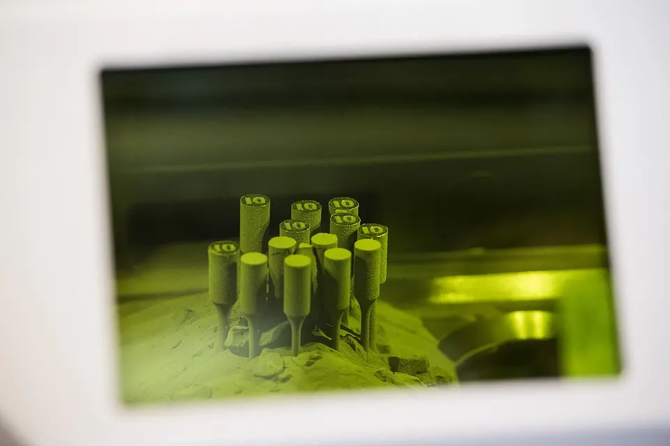 Looking through the window of a laser metal printer at parts growing in the powder bed; Skyfall scales the same process up to hundreds of lasers