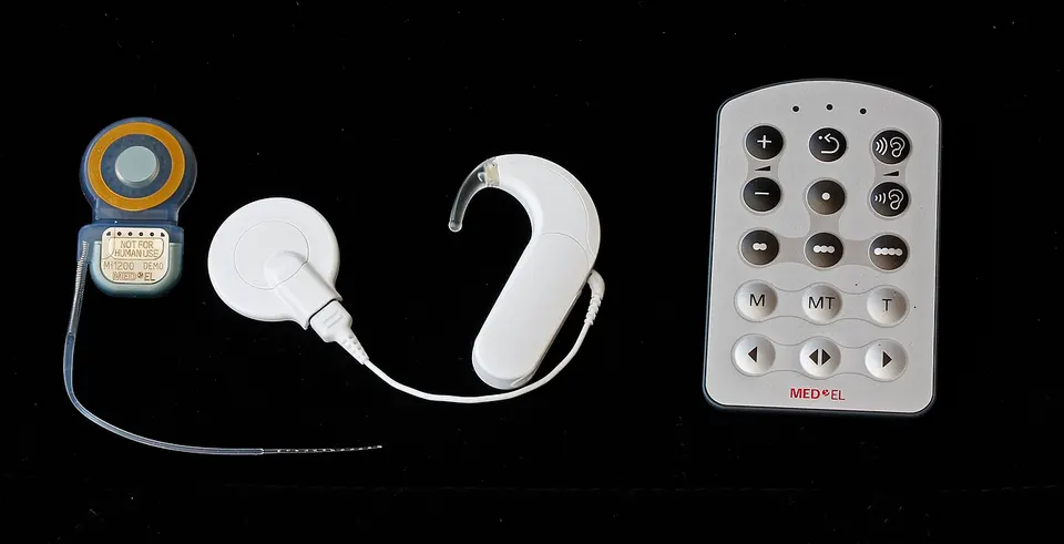 A cochlear implant (left) with its outer coil and processor: like the DOT, it sits under the scalp and gets power wirelessly through the skin