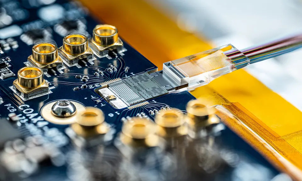 A PsiQuantum photonic chip on its test board, with a ribbon of optical fibres coupled to its edge to carry photons on and off the chip