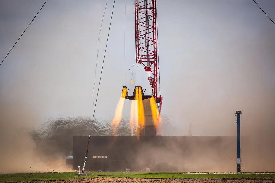 A Crew Dragon test capsule hovering on its SuperDraco engines, which sit in pods built into the capsule's walls