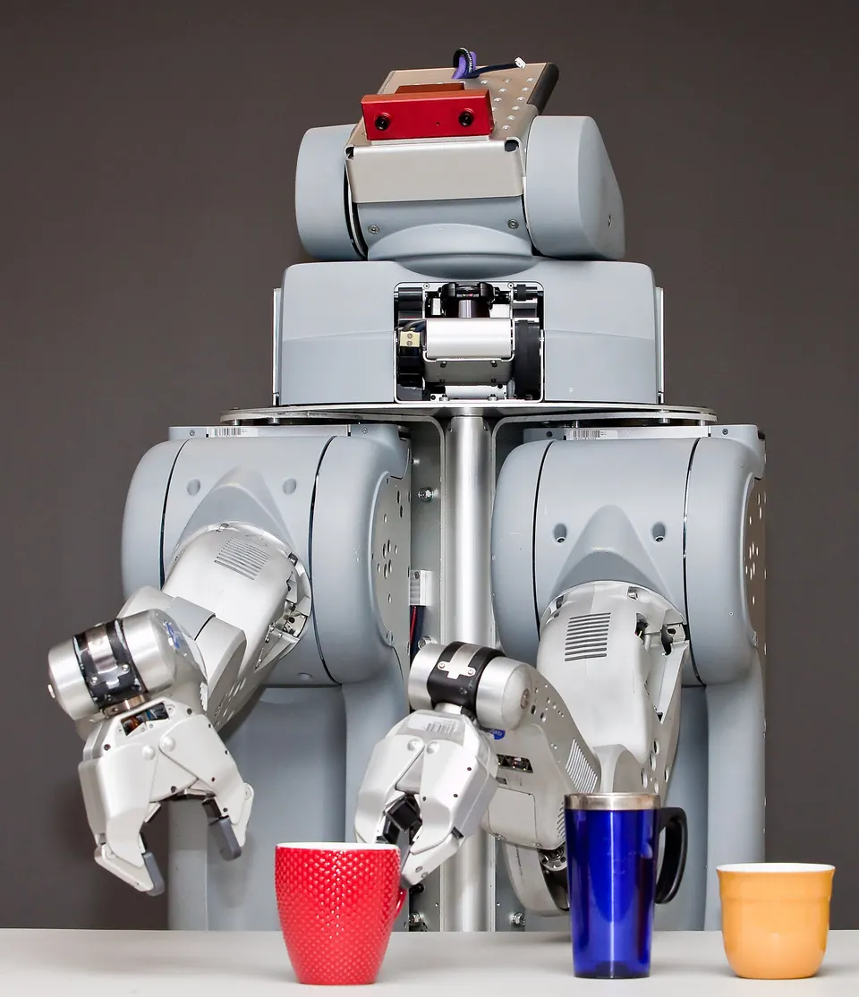 PR2, an earlier research robot, picking up cups with two gripper arms; The Bot Company's robot is unrevealed, but tidying needs the same skills