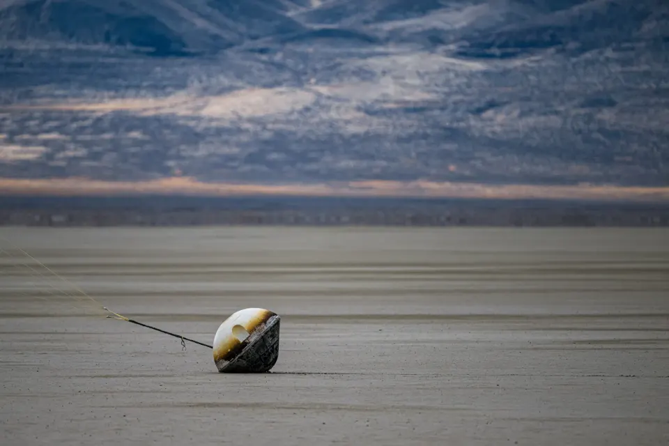 Varda's W-1 capsule after landing in the Utah desert in 2024: its scorched heat shield took the hypersonic reentry, the parachute lines trail left