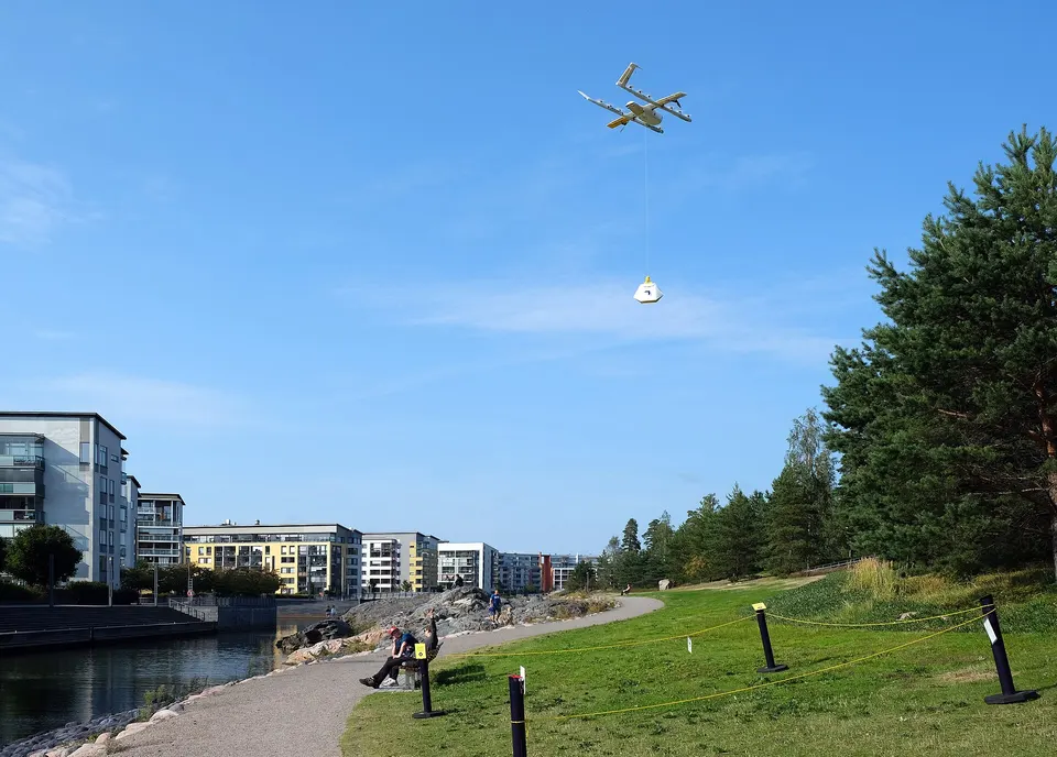 A Wing drone hovering over a Helsinki park and lowering a parcel on a tether, so it never has to land